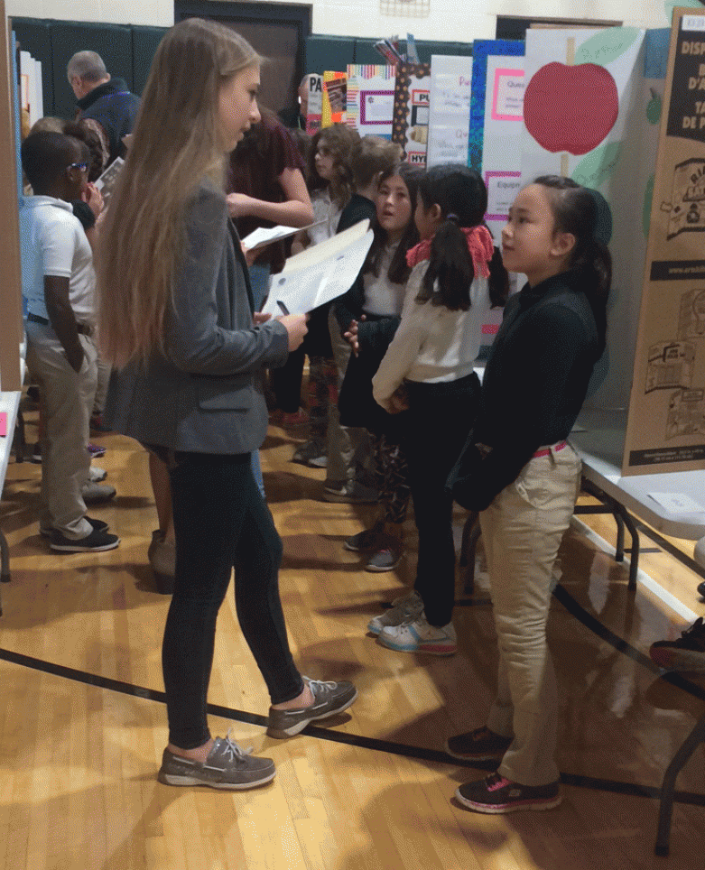 Penn student Lauren Frank interviews a Kennedy third-grader about her Science Fair project.