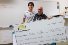 Two people posing with a large check in front of a classroom.