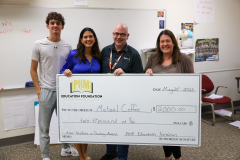 Three people posing with a check in front of them in an office setting.