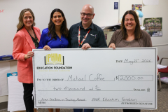 Three people standing in front of a large check. They are posing for a picture. The person on the left is holding a plaque.