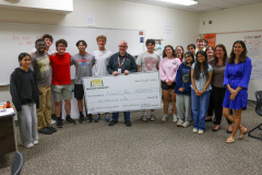 People posing around a check, celebrating an achievement in a classroom setting.
