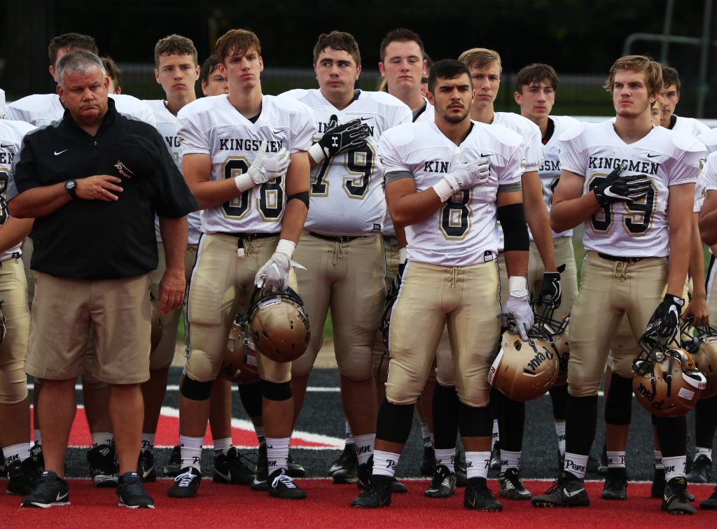 Penn Football Head Coach Cory Yeoman and Kingsmen players stand at attention for the playing of the National Anthem.