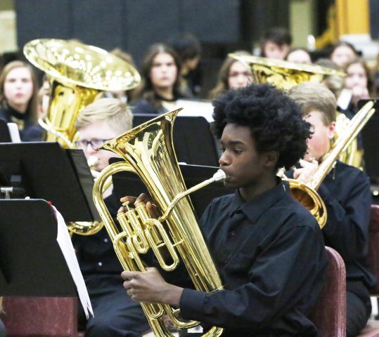 A young man playing a tuba in a band.