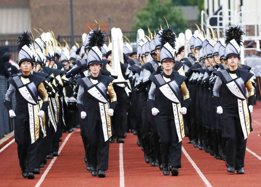 Parade band members in uniform marching down a street.