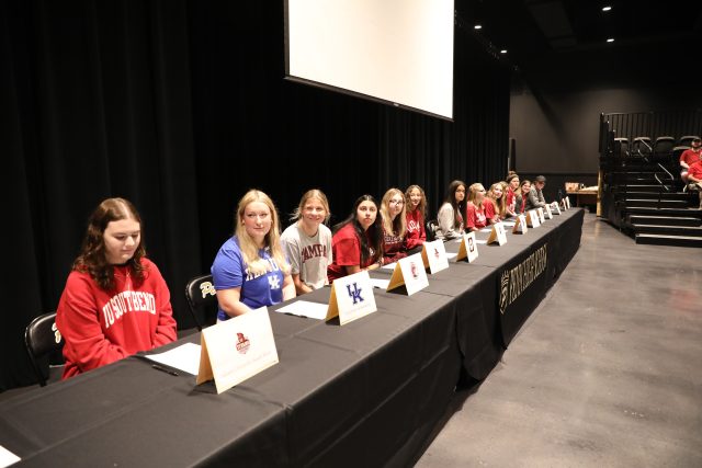 Students seated at a table in front of a stage, posing for a group photo.