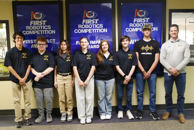 Team of robotics competition participants posing for a picture in front of a sign.