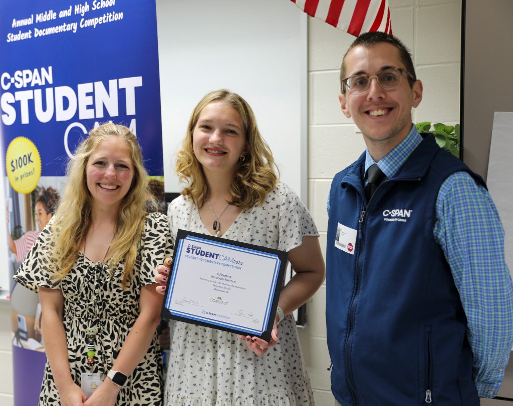 Student standing in middle holding C-SPAN award with teacher and man from C-SPAN alongside her