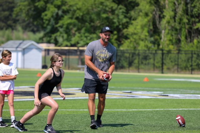 Man in black shirt throwing football to child on field.