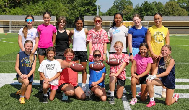 A group of young women posing for a team photo on a football field.