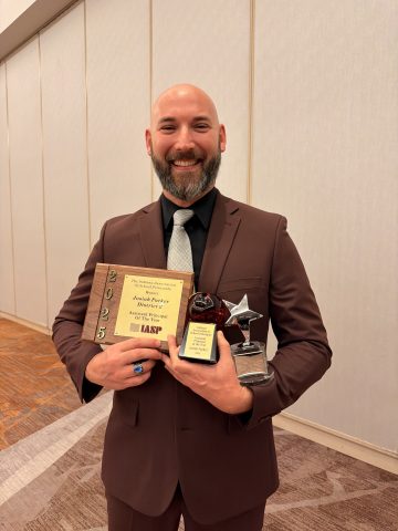 Man in suit holding awards, standing indoors.