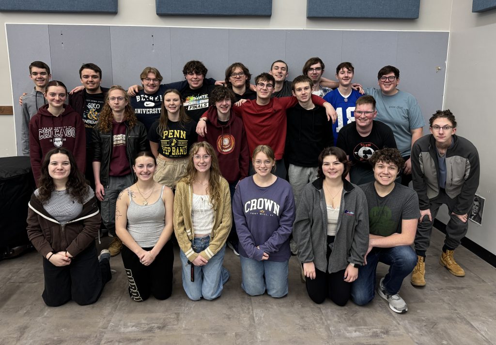 Group of people posing for a picture in front of a stage, smiling and looking at the camera.