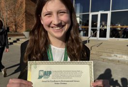 Girl holding a certificate in front of a building.
