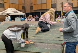 People working on a roof, one person is standing on top of the roof while others are working underneath.