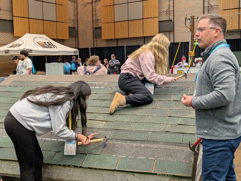 People working on a roof, one person is standing on top of the roof while others are working underneath.