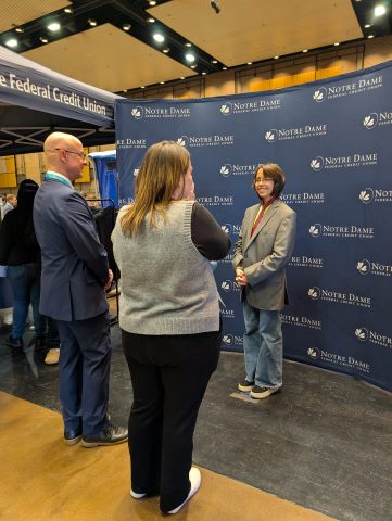 People standing in front of a booth at an event, engaging in conversation.