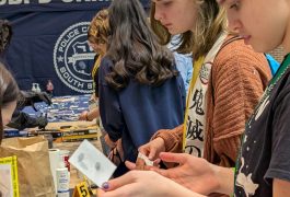 People gathered around a table at an event, examining items on display, including a badge and a sign that reads "BPD Crime