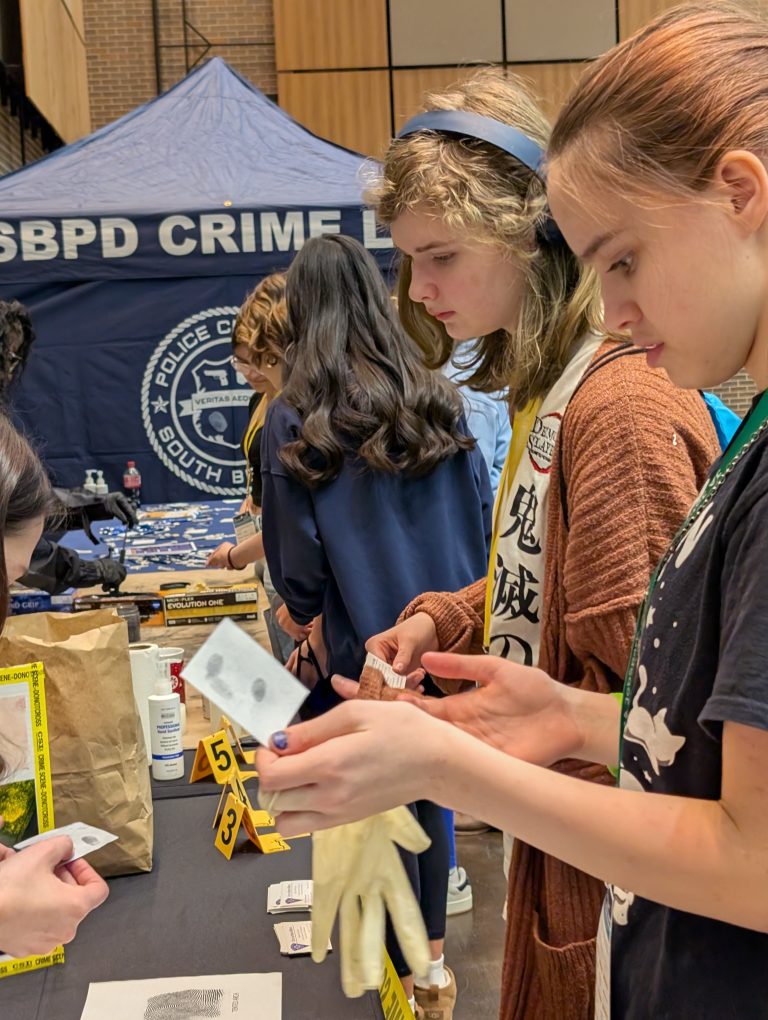 People gathered around a table at an event, examining items on display, including a badge and a sign that reads "BPD Crime