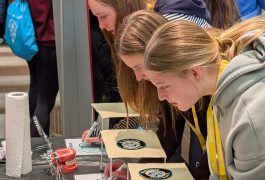 People gathered around a table at an event, looking at items on display, possibly signing up for something or writing on