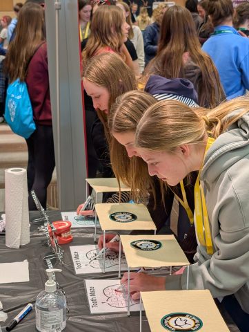 People gathered around a table at an event, looking at items on display, possibly signing up for something or writing on