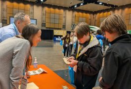 People standing around a table with papers on it at an event.