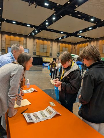 People standing around a table with papers on it at an event.