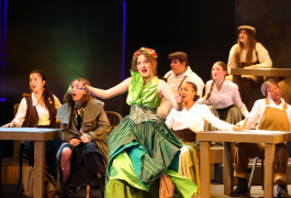 Theatrical performance of a woman in a green dress dancing on stage, surrounded by other performers and set against a