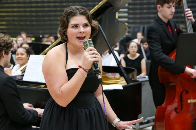 Woman in a black dress singing into a microphone on stage.