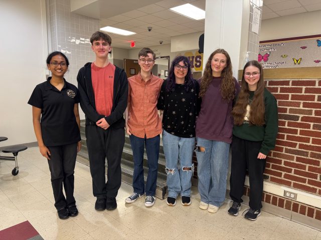 Group of people posing in front of a brick wall, at a school