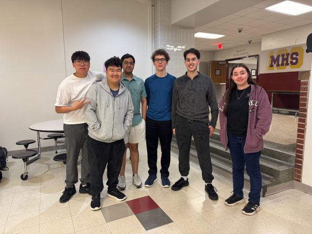 Group of young people posing in front of school building.