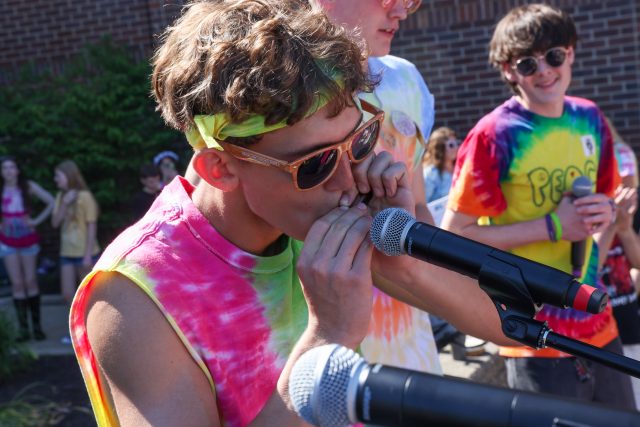 Man in tie-dye shirt holding microphone to mouth, singing passionately.