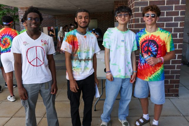 Four young men in colorful tie-dye shirts posing for a picture at an event.