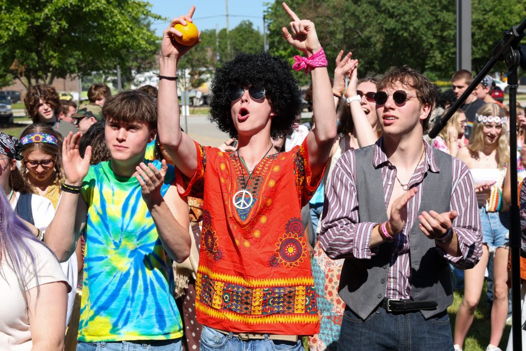 People in colorful tie-dye shirts performing on stage at a festival.