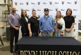 Five people posing in front of a banner for Penn High School.