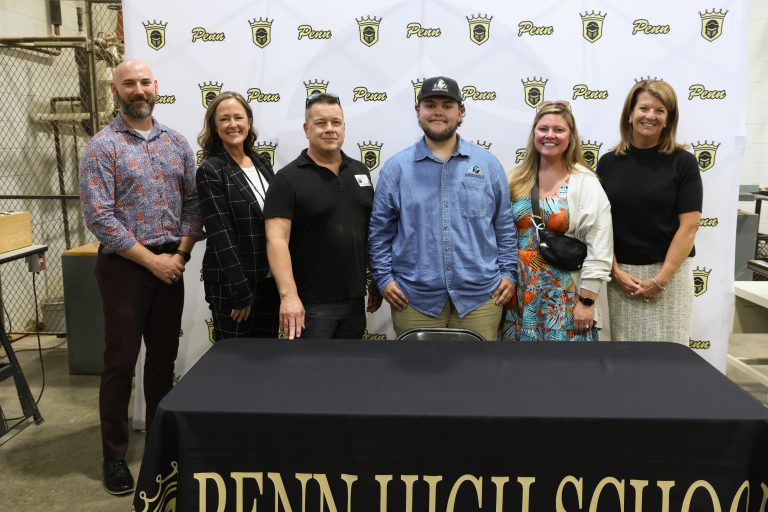 Five people posing in front of a banner for Penn High School.