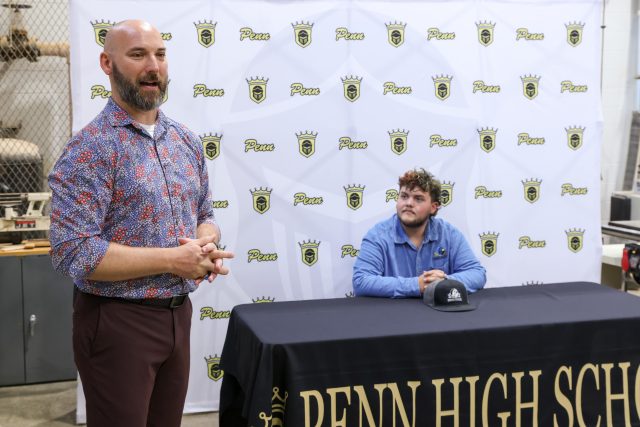 Man standing next to a table with a sign that says "PENN HIGH SCHOOL" and another sign that reads "PENN HIGH SCH