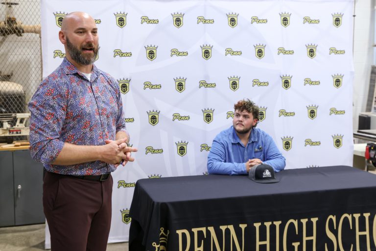 Man standing next to a table with a sign that says "PENN HIGH SCHOOL" and another sign that reads "PENN HIGH SCH