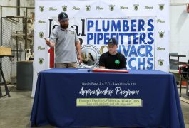 Two men at a table with a sign that reads "Plumbers Pipefitters WAC".