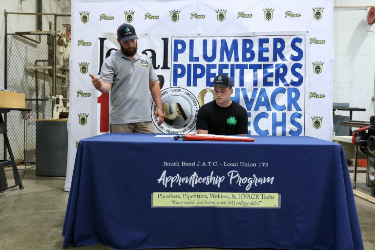 Two men at a table with a sign that reads "Plumbers Pipefitters WAC".