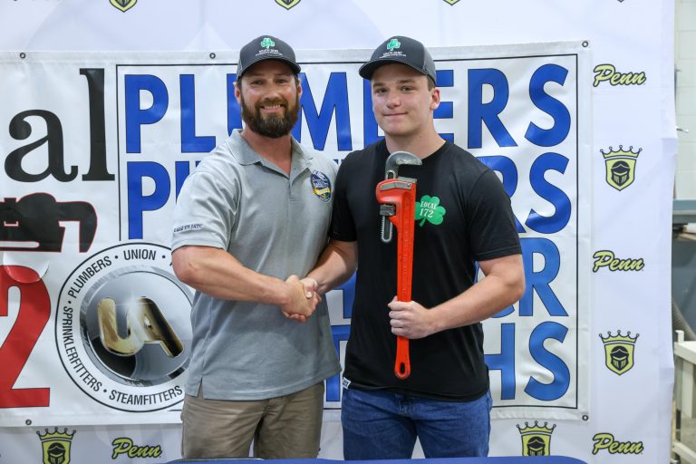 Two men shaking hands in front of a sign that says "2023 Union Plumbers".