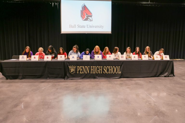 The group of people is seated at a table, possibly in an educational setting, where they are signing papers.