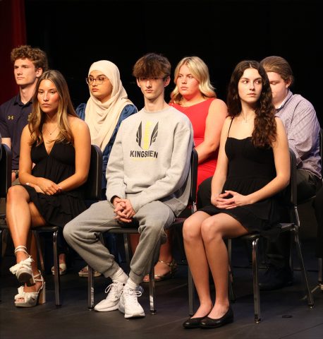 Group of young people sitting in a row on stage, posing for a picture.