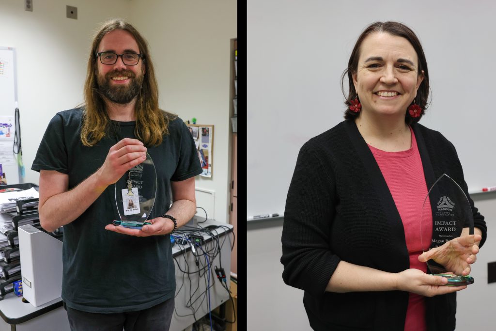 Two people holding awards in a room, one person on left is bearded, both smiling and looking at the camera.