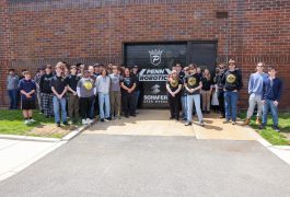 A group of people posing in front of a building with a sign that says "PENN ROBOTICS" and a logo for a robotics team.