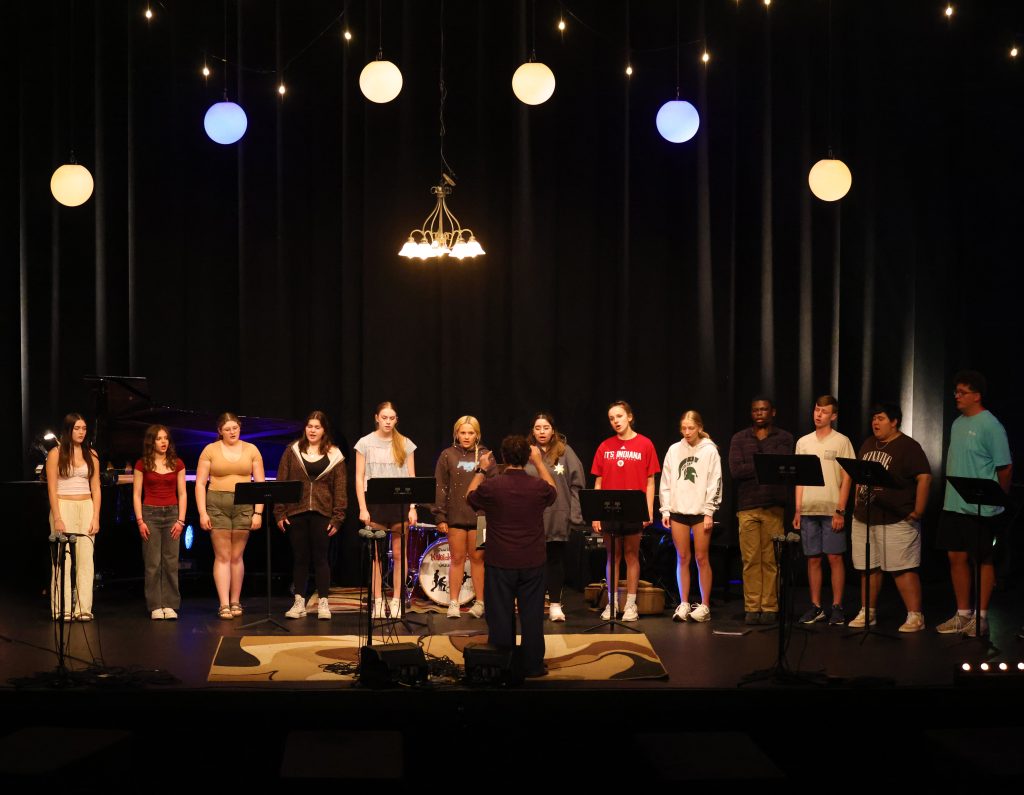 Choir members on stage, singing in front of microphones.