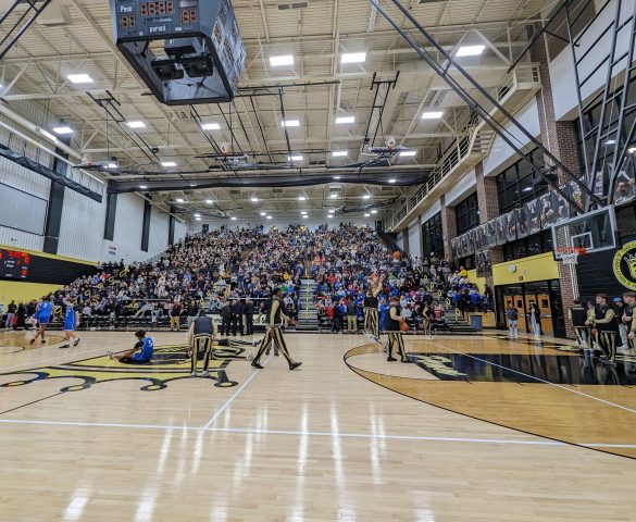 Spectators gathered in gymnasium for basketball game.