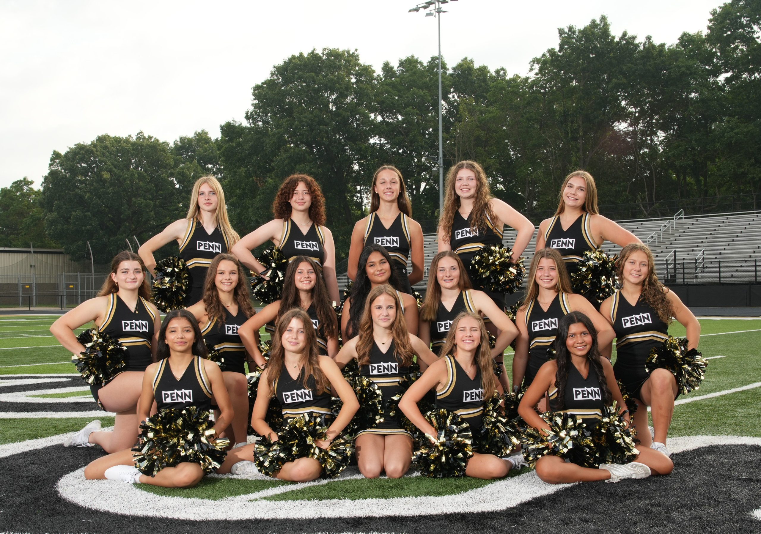 A group of cheerleaders posing for a team picture on a football field.