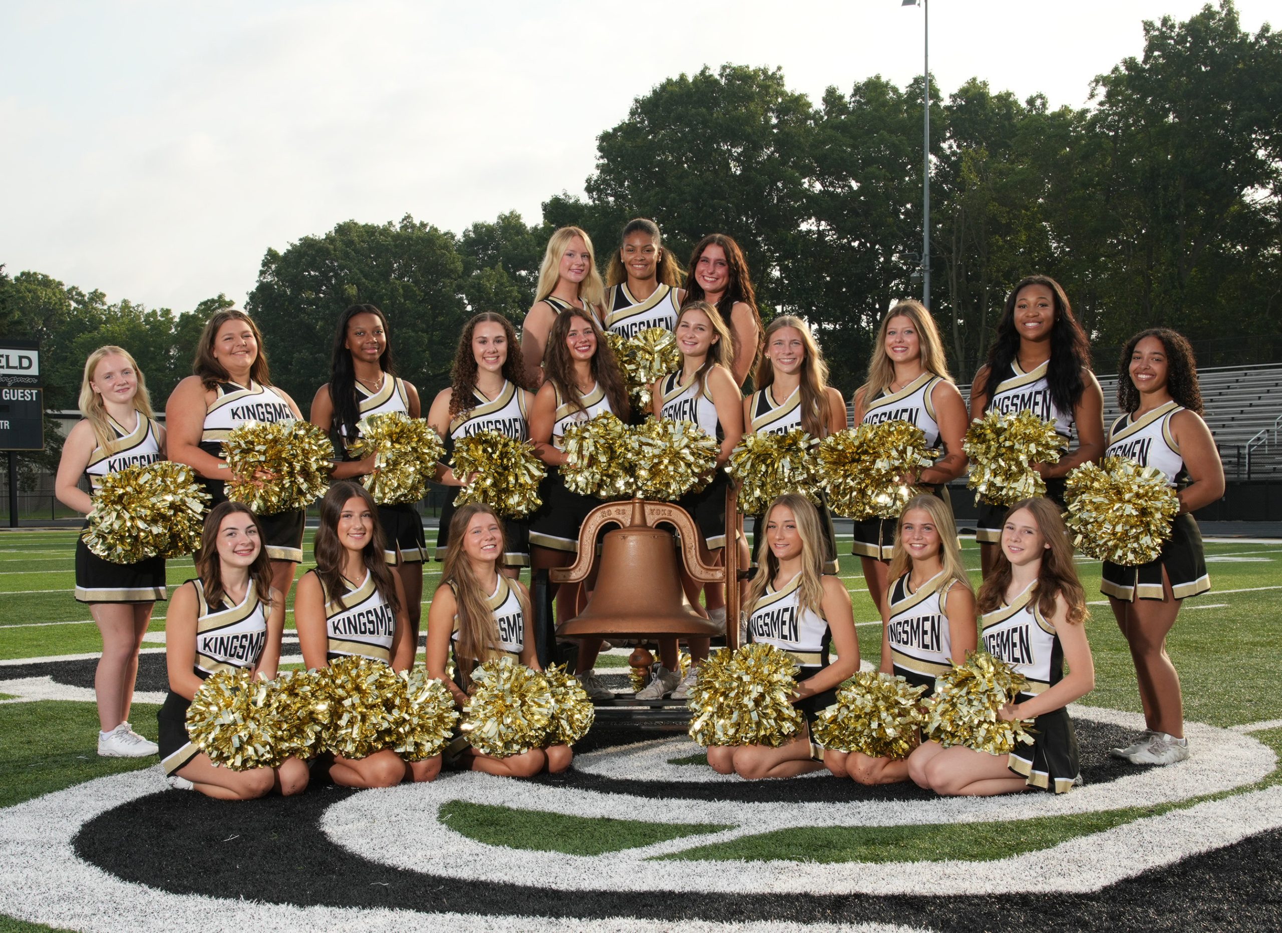 The cheerleaders are posing for a team photo at a football stadium.