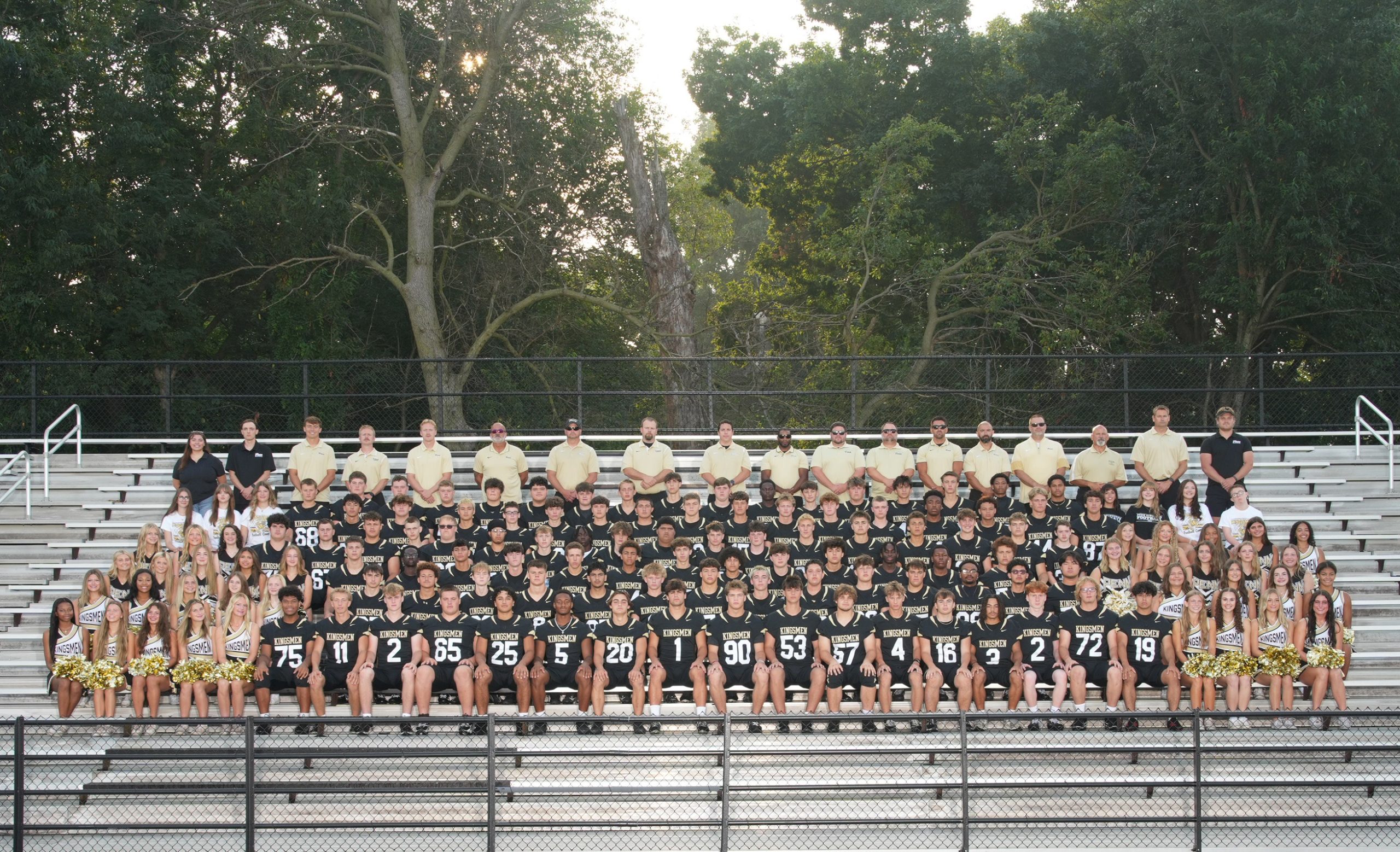 Team posing on bleachers at a football game.