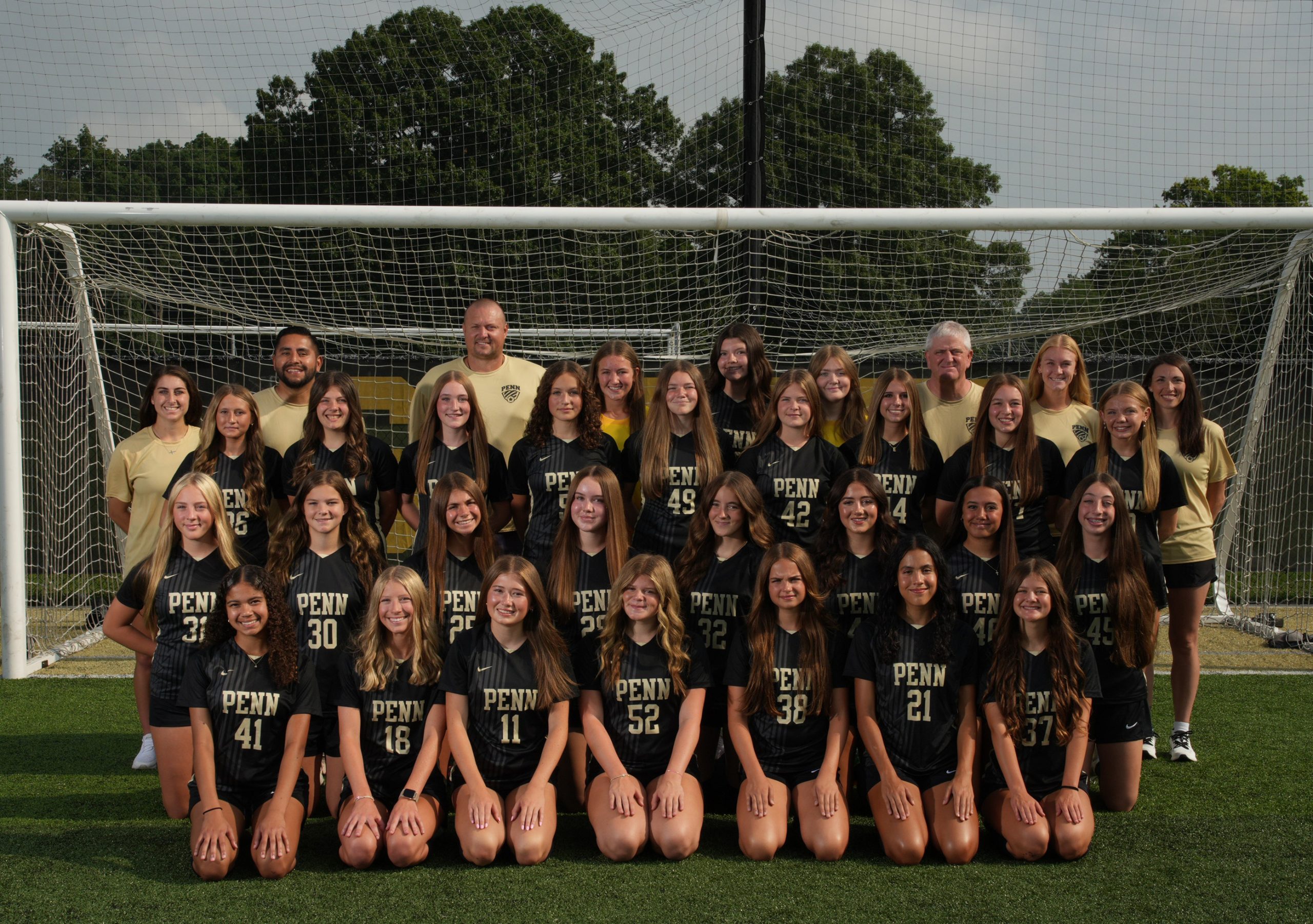 Team of young women posing in front of a soccer goal.