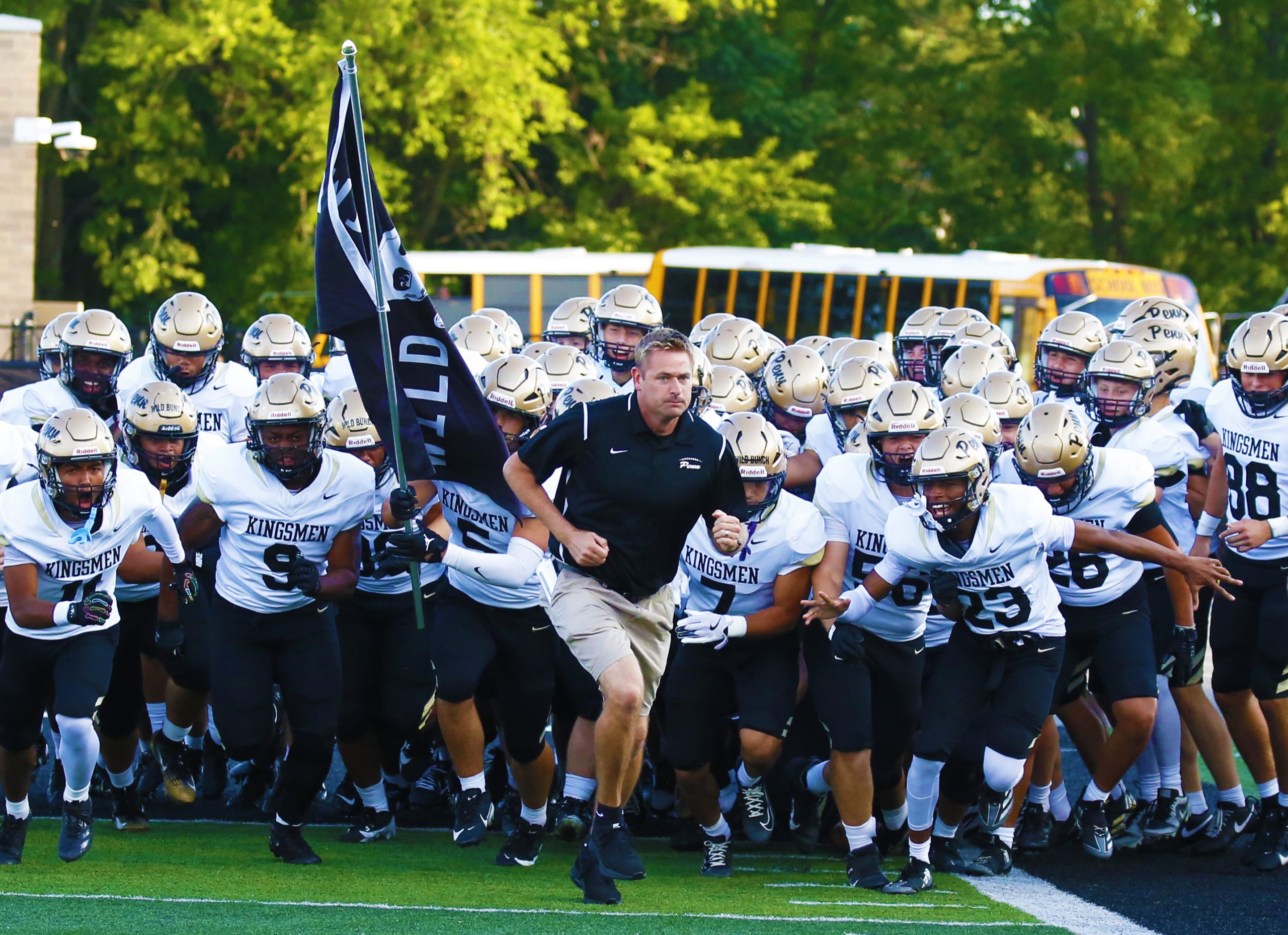 Football team on field holding flag, coach running with them.